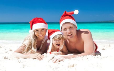 Man, woman and child laying on the beach wearing santa hats
