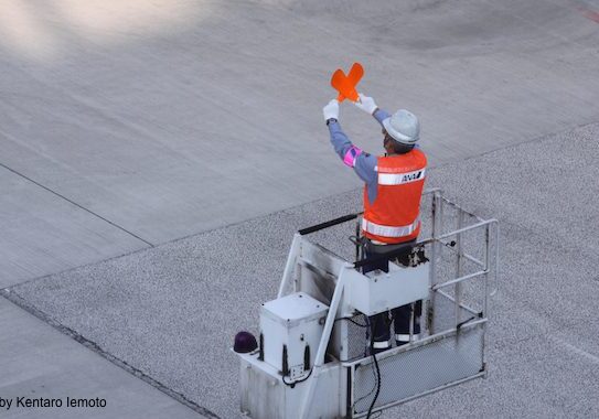 Airport worker signaling on tarmac platform.