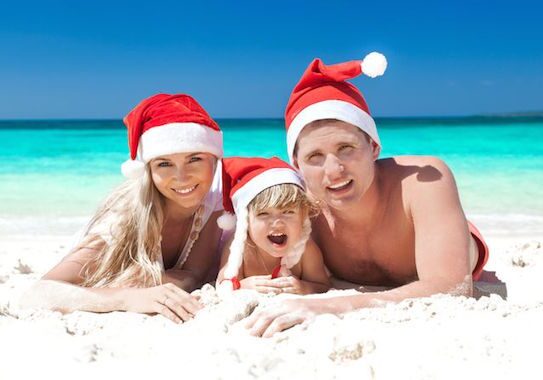 Family wearing Santa hats on tropical beach.